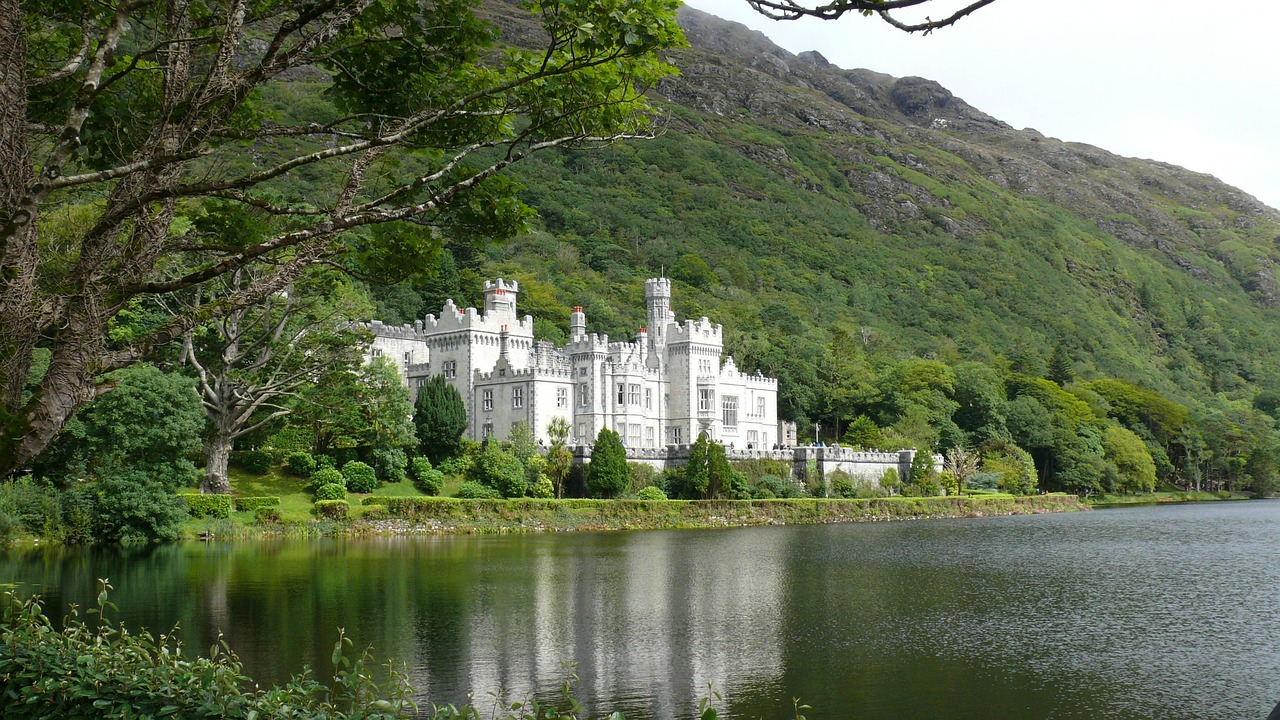 Kylemore-style castle by a lake with mountains behind